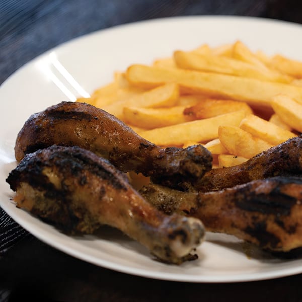 Four grilled chicken drumsticks with crispy skin and a side of golden french fries on a white plate.
