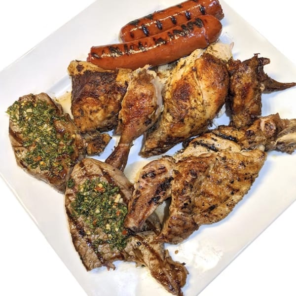 Grilled chicken pieces, two sausages, and two steaks with green sauce on a white platter.