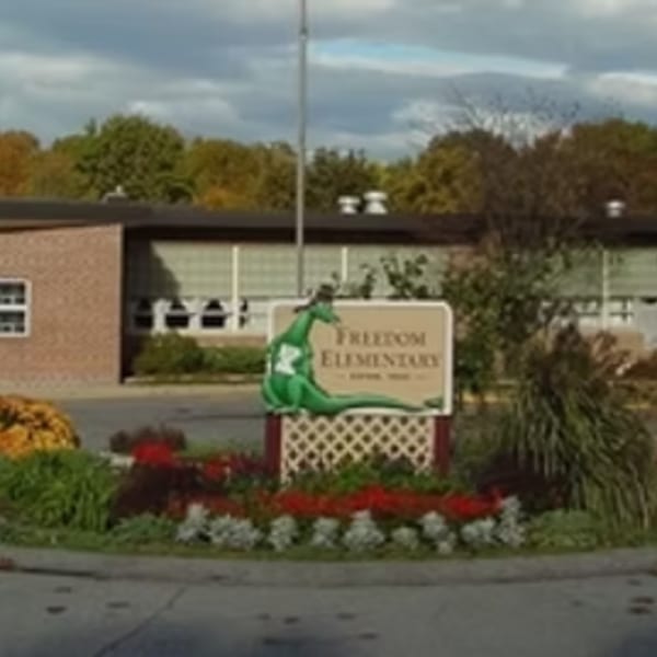 A school sign for "Freedom Elementary" with a green dragon statue in front of a brick building.