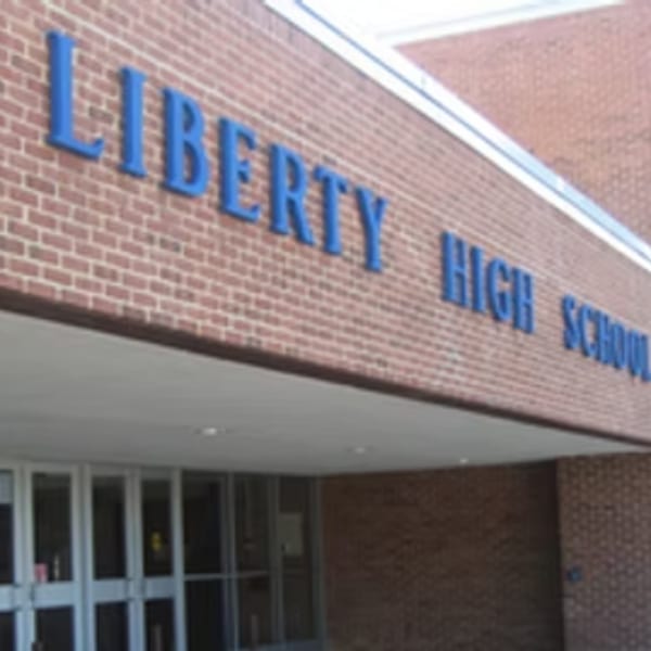 The entrance to Liberty High School, with blue letters on a brick wall above glass doors.