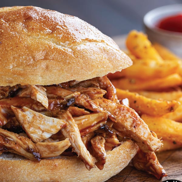 Mr. Jack's Peruvian Rotisserie Chicken sandwich with fries and ketchup on a wooden board.
