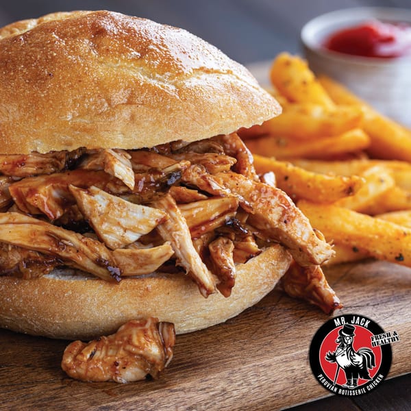Mr. Jack's Peruvian Rotisserie Chicken sandwich with fries and ketchup on a wooden board.